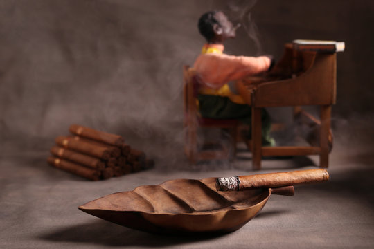 SMOKY HAVANA CIGARS  IN A WOODEN ASHTRAY NEXT TO A CIGAR ROLLER AND A CIGARS STACKING