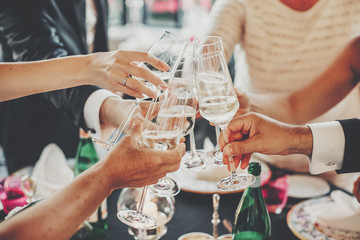 Hands toasting with champagne glasses at wedding reception outdoors in the evening. Family and...