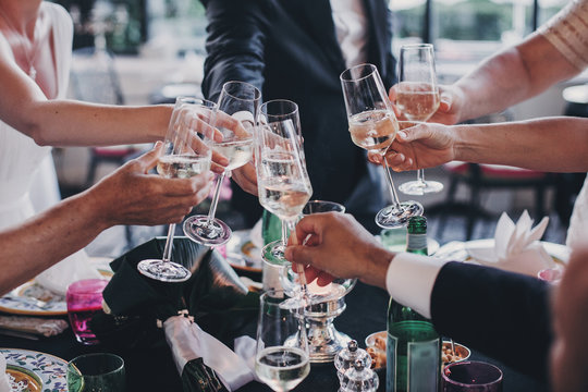 Group of people holding champagne glasses and toasting at wedding reception outdoors in the evening. Family and friends clinking glasses and cheering with alcohol at delicious feast celebration