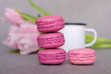 Sweet french macarons, cup of tea or coffee and spring flowers on grey background