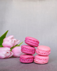 Stack of pink and purple french macarons and blooming tulips on gray background. Space for text
