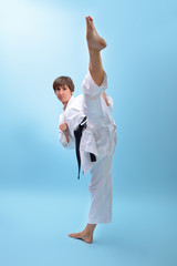 Obraz na płótnie Canvas Young karate woman in a white kimono with black belt demonstrates fighting stances and strikes. Girl at studio shows martial arts