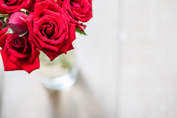 Close up of red rose bouquet in the vase on white wooden background