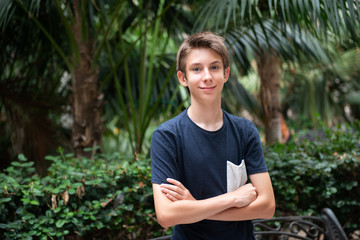 Young boy posing in summer park with palm trees. Cute spectacled smiling happy teen boy 13 years...