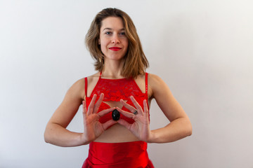 Woman in red lingerie holds jade egg. A confident young Caucasian female is seen wearing elegant red undergarments, holding a black love egg, used as an alternative health therapy in women.