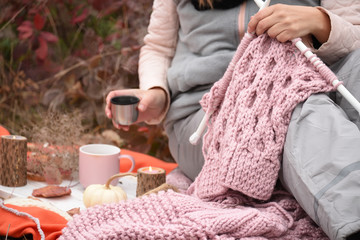 Hands knit needles fluffy pink knitting. The process of knitting in the autumn beautiful garden.