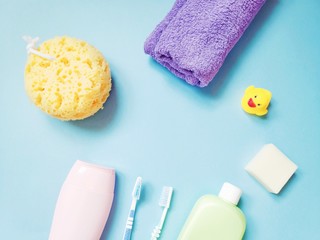 Shampoo, yellow sponge, toothbrushes, purple towel, shower gel, soap bar and yellow rubber duck. Bathroom items flat lay photo