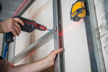 Male worker works with profile for drywall, setting, assembling with drill. Construction work,...
