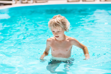 Curly boy enjoying sun and swimming in pool