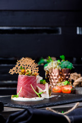 Beautiful serving of slice salted tuna with vegetables in a creamy sauce on a dark plate on a rustic wooden tray