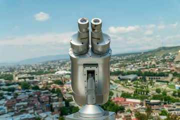 Binoculars close-up overlooking Tbilisi, the Georgian capital in the background on a sunny day. Gray device for sightseeing, stationary viewing of binoculars, viewing binoculars with bill acceptor.