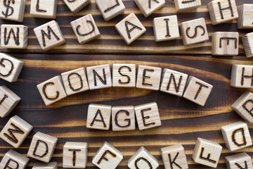consent age wooden cubes with letters, sexual education concept, around the cubes random letters, top view on wooden background