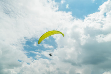 man on a yellow paraglider flying against the sky with clouds on a sunny day. Paraglider is flying against the sky with clouds. Paragliding in Georgia.