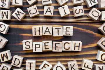 hate speech wooden cubes with letters, attacks a person or a group violence concept, around the cubes random letters, top view on wooden background