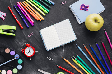 Naklejka premium Bright stationery, clock and apple around notebook on grey background