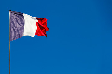 Fabric textile tricolor flag of France with blue, white and red stripes fluttering in the wind with copy space in sunny day with blue sky background