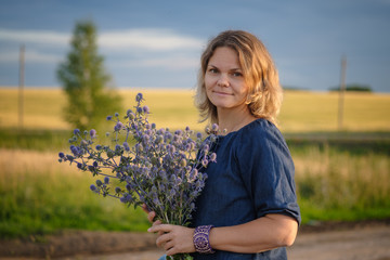 Naklejka na ściany i meble portrait of a young woman with a bouquet of thistles on a barley field on a summer evening at sunset