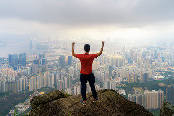An Asian tourist man hiking and looking at city on rock, mountain hill in Hong Kong downtown in...