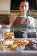 Pretty smiling female worker selecting muffins from a counter display in small bakery to sell to a customer, Family business concept