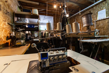 Overlock in a small sewing workshop. A retro overlock machine with spools of thread is seen inside a rustic fashion studio. Tools and workplace of a local eco designer.