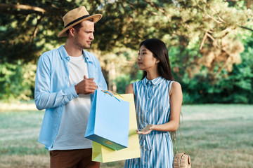 Naklejka premium happy young couple with shopping bags in the park