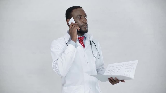 handsome african american doctor talking on smartphone and smiling while holding foder with diagnosis