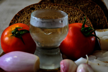 Freshly baked bread on a wooden cutting board with bacon, tomatoes, shot of vodka