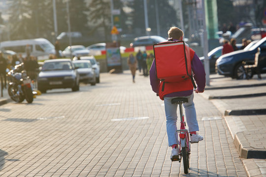 Young Boy On Bicycle Delivering Food In Boxes With Red Thermal Bag. Pizza Delivery Cyclist Carries Isothermal Backpack. Food Delivery In Any Weather Around The Clock. Food Delivery Or Takeout