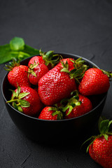 Heap of fresh strawberries and mint leaves in black bowl on dark background. top view