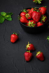 Heap of fresh strawberries and mint leaves in black bowl on dark background. top view