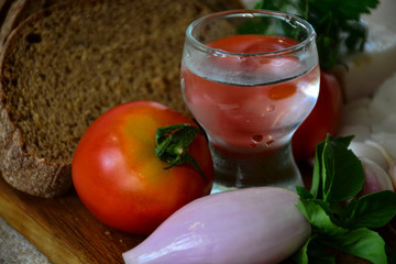  Freshly baked bread on a wooden cutting board with bacon, tomatoes, onions, garlic, basil and a shot of vodka
