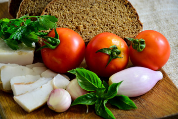 Freshly baked bread on a wooden cutting board with bacon, tomatoes, onions, garlic and basil