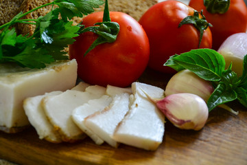 Freshly baked bread on a wooden cutting board with bacon, tomatoes, onions, garlic and basil