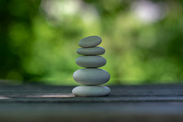 Obraz na płótnie Canvas Harmony and balance, cairns, simple poise pebbles on wooden table, natural green background, simplicity rock zen sculpture
