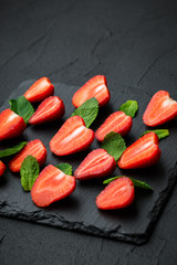 sliced fresh strawberries and mint leaves. dark stone background. 