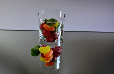 Multicolored tasty candies in a glass cup on the mirror. The reflection of the glass and sweets creates a striking effect of volume and increases the number of objects in the frame, which makes sweets