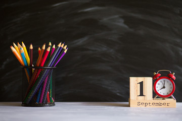 Concept back to school. Re alarm clock with color pencils and wooden calendar set on 1st september on black blackboard background. Design copy space supplies