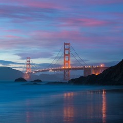 Fototapeta na wymiar Classic panoramic view of famous Golden Gate Bridge seen from scenic Baker Beach in beautiful golden evening light on a dusk with blue sky and clouds in summer, San Francisco, California, USA