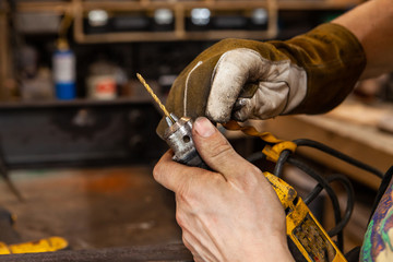 Obraz premium Blacksmith changing a drill bit. A closeup view on the dirty hands of a metalworker using the chuck of a power drill to replace a spotting bit, used for marking and drilling holes in steel.