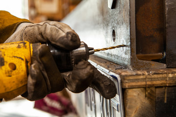 Metalworker drills starter hole in steel. A close up shot of a blacksmith wearing protective gloves whilst drilling a hole through a thick piece of metal. Spotting drill bit used for marking steel.