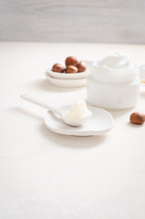 Shea butter in ceramic spoon on white background with nuts and moisturizer creme. Free text space.