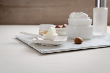 Shea butter in ceramic spoon on white background with nuts and moisturizer creme. Free text space.