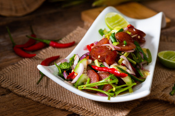 Spicy Chinese pork sausage with vegetable Thai salad in white plate on wood background
