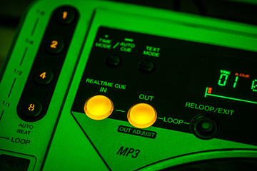 Closeup of 'Cue IN/OUT' buttons on a CD Player. Green stage lighting.