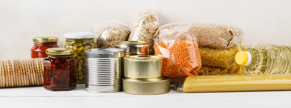 Various canned food and raw cereal grains on a table.