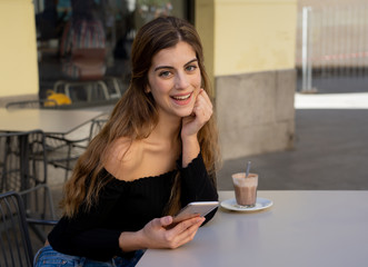 Attractive young woman chatting and dating on smart mobile phone in coffee shop outside city street