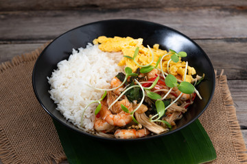 Rice topped with stir-fried shrimp and basil, and fried eggs in white dish.