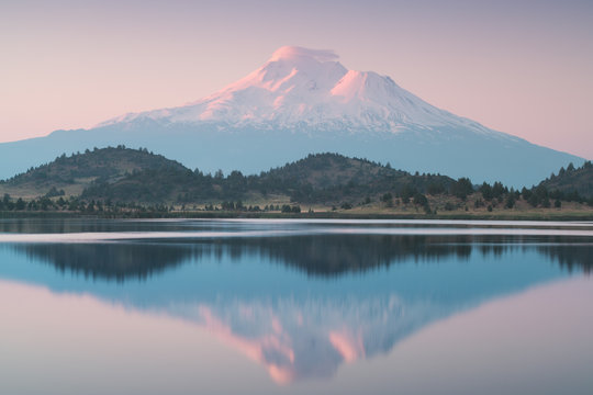 A reflection of snow capped Mount Shasta in a clear water in lake  at sunrise in California State, USA.  Mount Shasta is a volcano at the southern end of the Cascade Range in Siskiyou County 