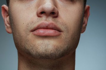 Close-up portrait of young man isolated on grey studio background. Caucasian male model's face and lips. Concept of men's health and beauty, self-care, body and skin care.