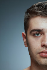 Naklejka premium Close-up portrait of young man isolated on grey studio background. Caucasian male model looking at camera and posing, looks serious. Concept of men's health and beauty, self-care, body and skin care.